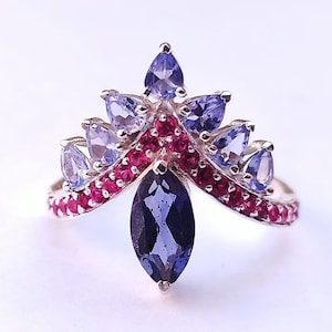 Puede incluir: Un anillo de plata con una gran piedra preciosa de forma marquesa azul oscuro rodeada de piedras más pequeñas azules y rojas.