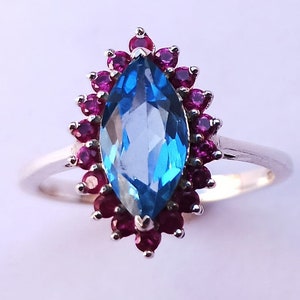 May include: A silver ring with a large blue topaz gemstone surrounded by a halo of smaller red rubies.