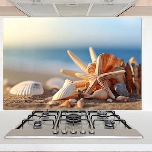 Puede incluir: Un protector contra salpicaduras de cocina decorativo con una escena de playa con conchas marinas y una estrella de mar. La imagen muestra una variedad de conchas marinas, una estrella de mar y pequeñas rocas en una playa arenosa con el océano al fondo.