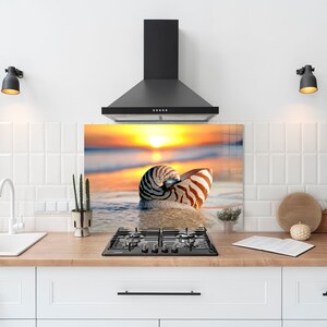 May include: A kitchen backsplash with a sunset and seashell design. The backsplash is made of tempered glass and features a nautilus shell on a beach at sunset.