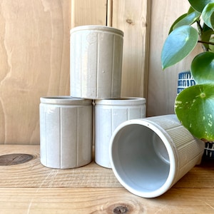 May include: Four white ceramic jars with vertical lines stacked on a wooden surface. The jars are all the same size and shape.