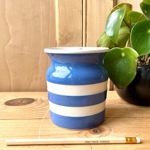 May include: A blue and white striped ceramic jar with a white lid. The jar is sitting on a wooden surface with a pencil that says "ONLY NICE THINGS" on it.