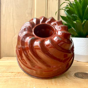 Peut inclure: Moule à gâteau bundt en métal rouge avec un design cannelé. Le moule est légèrement usé et a une finition brillante.