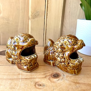 May include: Two brown ceramic lion figurines with open mouths and intricate details. The figurines are traditional Chinese guardian lions, also known as foo dogs.