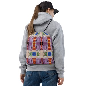 May include: A drawstring bag with a colorful pattern featuring a repeated image of a person in a pink dress. The pattern also includes red, yellow, green, and blue stripes.