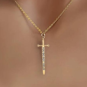 Puede incluir: Collar de oro con un colgante de espada que dice "You Do Not Yield".