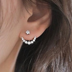 以下が含まれることがあります： 三日月型のデザインのシルバー製のイヤリングのペア。イヤリングは、小さな透明なキュービックジルコニアの石で飾られています。イヤリングは、耳の上部に着用するように設計されており、三日月型が耳たぶから外側に伸びています。