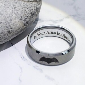 May include: A silver tungsten carbide ring with a black bat design and the inscription "In Your Arms Im Home".