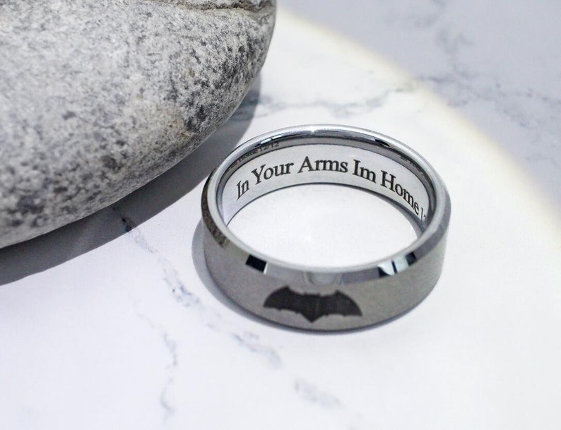 May include: A silver tungsten carbide ring with a black bat design and the inscription "In Your Arms Im Home".