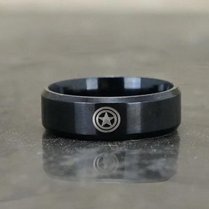 May include: A black ring with a silver star inside a circle design.