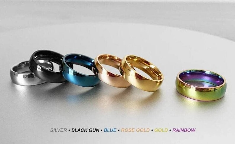 May include: Six different colored metal rings, from left to right: silver, black, blue, rose gold, gold, and rainbow.