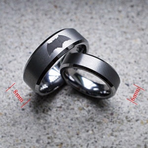 May include: Two tungsten carbide rings with a black matte finish. The wider ring is 8mm wide and features a Batman logo. The narrower ring is 6mm wide.