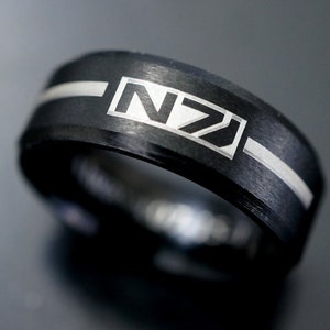 Puede incluir: Un anillo negro con una banda plateada y las letras "NZ" grabadas en la parte superior.