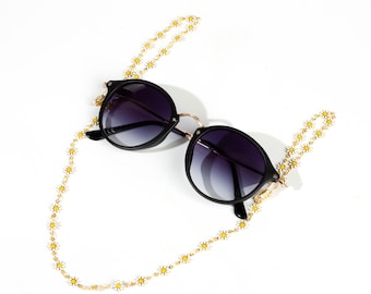 May include: Black round sunglasses with a gold frame and a daisy chain attached to the temples.