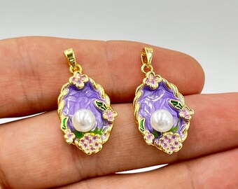 May include: Two gold-toned pendants with a floral design. Each pendant features a purple oval shape with a white pearl in the center, surrounded by pink and green floral accents. The pendants are designed for jewelry making.