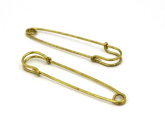 May include: Two gold safety pins, one larger than the other, on a white background.