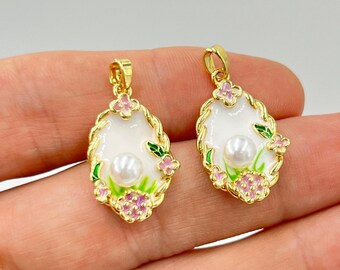 May include: Two gold-colored pendants with an oval shape. Each pendant features a white enamel base, a central pearl, and floral accents in pink and green. The edges are adorned with a twisted rope design.
