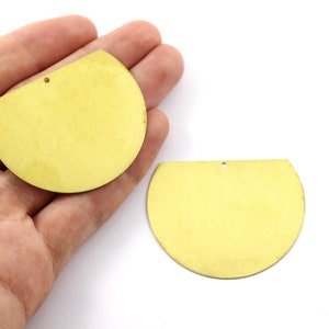 Op de afbeelding: Twee halfronde vormen van goudkleurig metaal met een gat in het midden. De vormen zijn ongeveer 5 cm in diameter.
