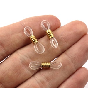 以下が含まれることがあります： 金色の金属製のアクセントが付いた透明なプラスチック製の眼鏡ストラップホルダー3個。ホルダーは眼鏡の腕の端に付けるように設計されています。