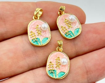 May include: Three gold-toned pendants with oval pink enamel backgrounds. Each pendant features a floral design with gold and green accents, and a white pearl. The pendants are designed for jewelry making.