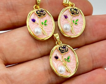 May include: Three gold-toned oval pendants with a pink enamel background. Each pendant features a black rose, purple accents, green leaves, and a white pearl. The pendants are held in a hand.