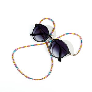 May include: Black round sunglasses with a colorful beaded strap. The strap is made of small beads in shades of pink, blue, and gold.