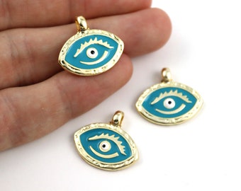 May include: Gold-colored metal pendants with a turquoise enamel eye design. The eye features a white iris and a black pupil. The pendants have a loop at the top for attaching to a chain or other jewelry. The pendants are oval-shaped.