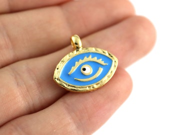 May include: Gold-toned pendant charm with a blue enamel eye design. The eye has a white pupil and a black center. The charm is shaped like an oval and has a textured edge.