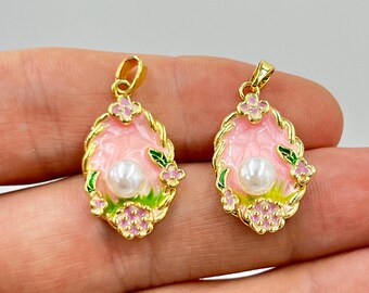 May include: Two gold-colored pendants with pink enamel centers and a faux pearl. The pendants have a floral design with pink flowers, green leaves, and a gold-colored rope-like border. The pendants are oval-shaped.