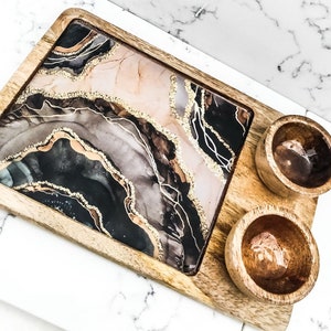 May include: A wooden serving tray with a black, gold, and pink resin inlay. The tray has two small wooden bowls.