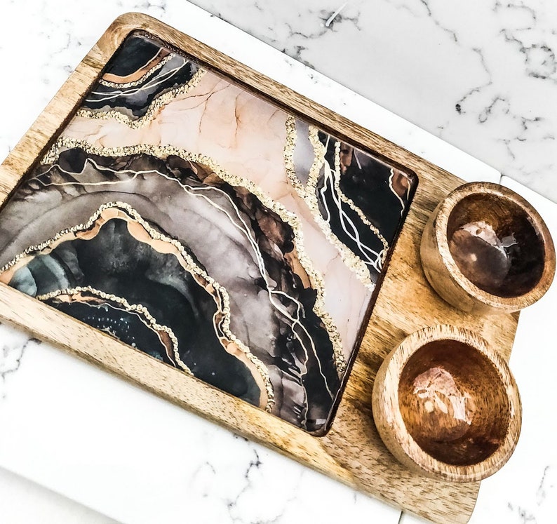 May include: A wooden serving tray with a black, gold, and pink resin inlay. The tray has two small wooden bowls.