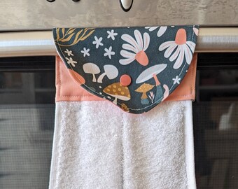Könnte beinhalten: Ein weißes Küchentuch mit einer grünen und rosa Stoffschlaufe, die an einem silbernen Backofengriff hängt. Die Stoffschlaufe hat einen floralen und Pilz-Druck.