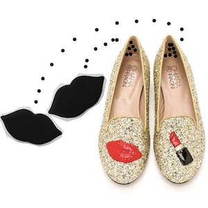 May include: A pair of gold glitter flats with red lips and lipstick designs. The shoes are by the brand "Chiara Ferragni".