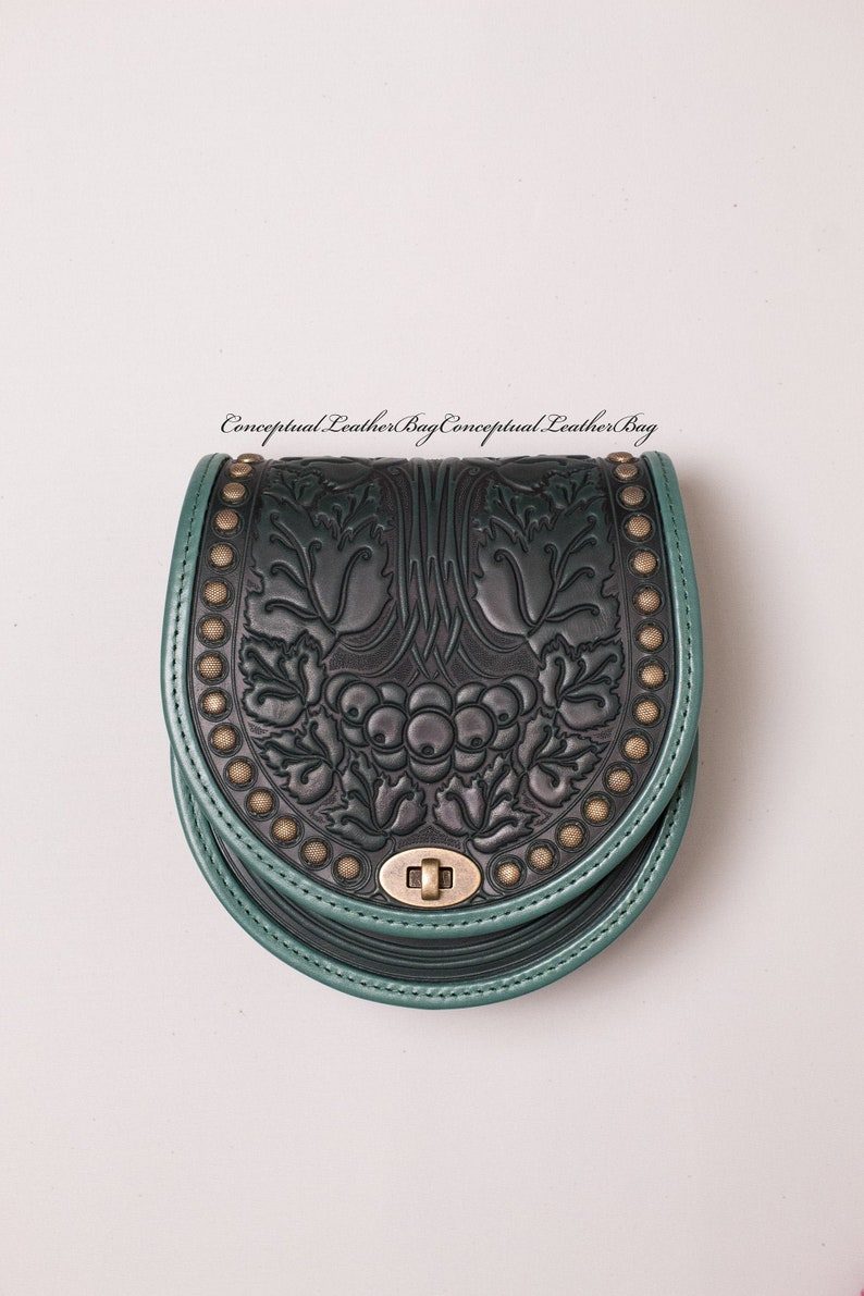 May include: A dark green leather bag with a black floral design and gold accents. The bag has a flap closure with a metal clasp.