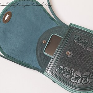 May include: A teal green leather crossbody bag with a flap closure and a decorative embossed design. The bag has a small pocket on the front and a larger pocket on the back. The bag is open and a phone is visible inside.