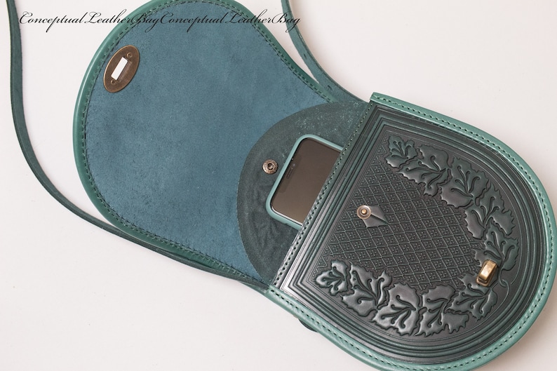 May include: A teal green leather crossbody bag with a flap closure and a decorative embossed design. The bag has a small pocket on the front and a larger pocket on the back. The bag is open and a phone is visible inside.