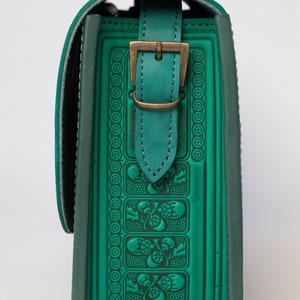 May include: A green leather shoulder bag with a decorative embossed pattern and a brass buckle. The bag has a flap closure and a strap.
