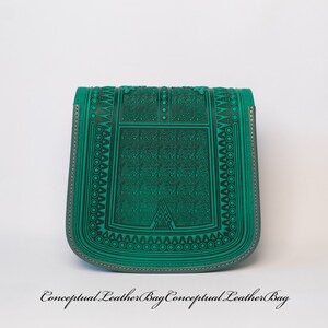 May include: A green leather bag with an intricate geometric pattern embossed on the front. The bag has a flap closure and a small strap.