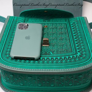 May include: A teal green leather bag with intricate embossed patterns. The bag is open and a teal green phone is inside. The bag has a strap and a metal clasp.
