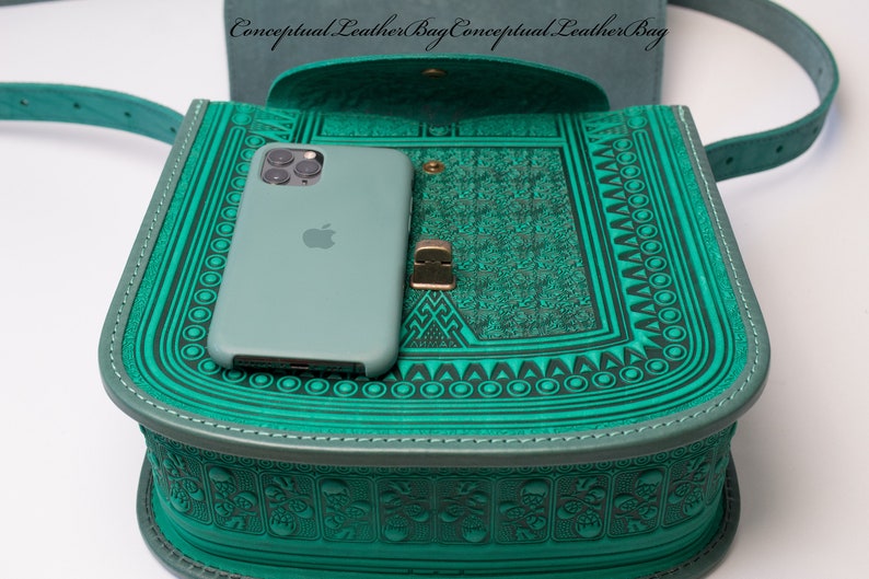 May include: A teal green leather bag with intricate embossed patterns. The bag is open and a teal green phone is inside. The bag has a strap and a metal clasp.