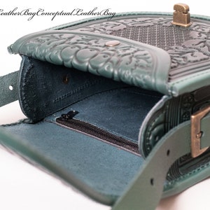 May include: A teal green leather bag with intricate embossed floral designs. The bag has a flap closure with a metal buckle and a zippered pocket on the inside.
