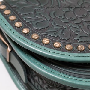 May include: Close-up of a dark green leather bag with a floral embossed design. The bag has a teal trim and gold-toned metal accents.