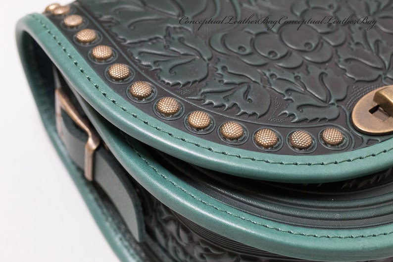 May include: Close-up of a dark green leather bag with a floral embossed design. The bag has a teal trim and gold-toned metal accents.