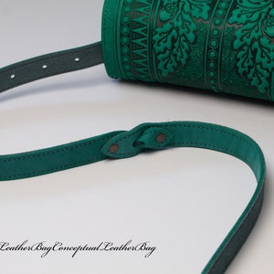 May include: A green leather shoulder bag with a decorative embossed pattern of leaves and acorns. The bag has a long adjustable strap.