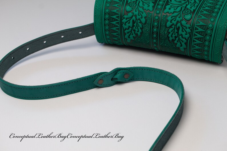 May include: A green leather shoulder bag with a decorative embossed pattern of leaves and acorns. The bag has a long adjustable strap.