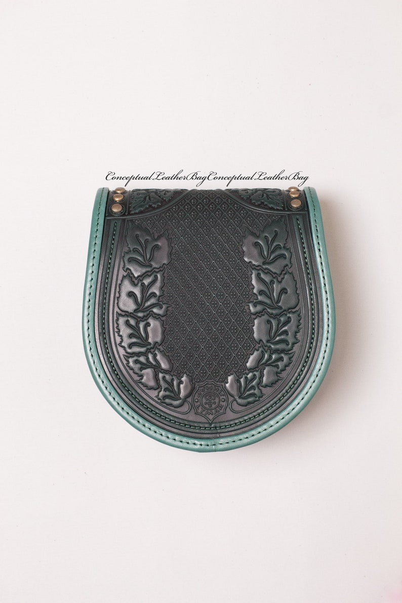 May include: A dark green leather bag with a decorative floral design and a green trim. The bag has a flap closure and a metal buckle.