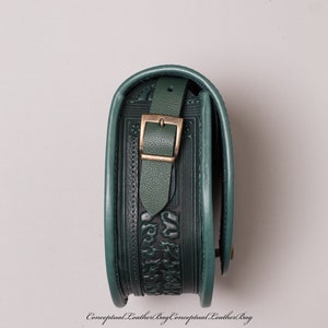 May include: A dark green leather bag with an embossed floral design and a brass buckle. The bag is closed and the strap is folded over the top.