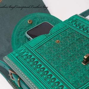 May include: A teal green leather shoulder bag with a geometric pattern and a flap closure. The bag has a small pocket on the front and a strap that can be adjusted. The bag is open and a smartphone is visible inside.