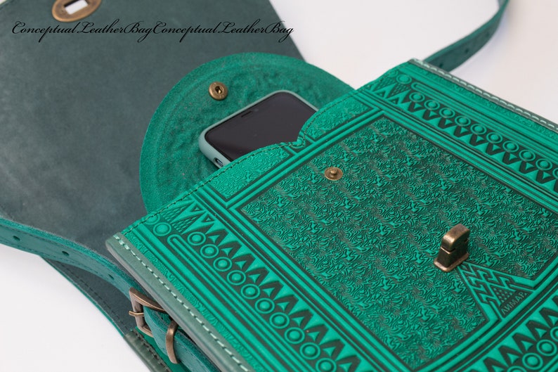 May include: A teal green leather shoulder bag with a geometric pattern and a flap closure. The bag has a small pocket on the front and a strap that can be adjusted. The bag is open and a smartphone is visible inside.