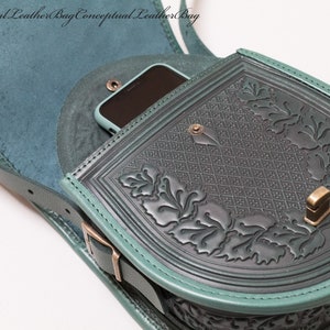 May include: A teal green leather satchel bag with a flap closure and a decorative floral design. The bag has a small pocket on the front that can fit a phone. The bag has a strap that can be adjusted to fit different body sizes.